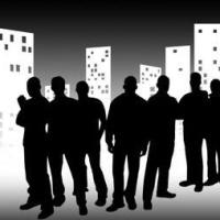 Die dunklen Silhouetten einer Gruppe von Menschen vor einer städtischen Skyline aus Hochhäusern.